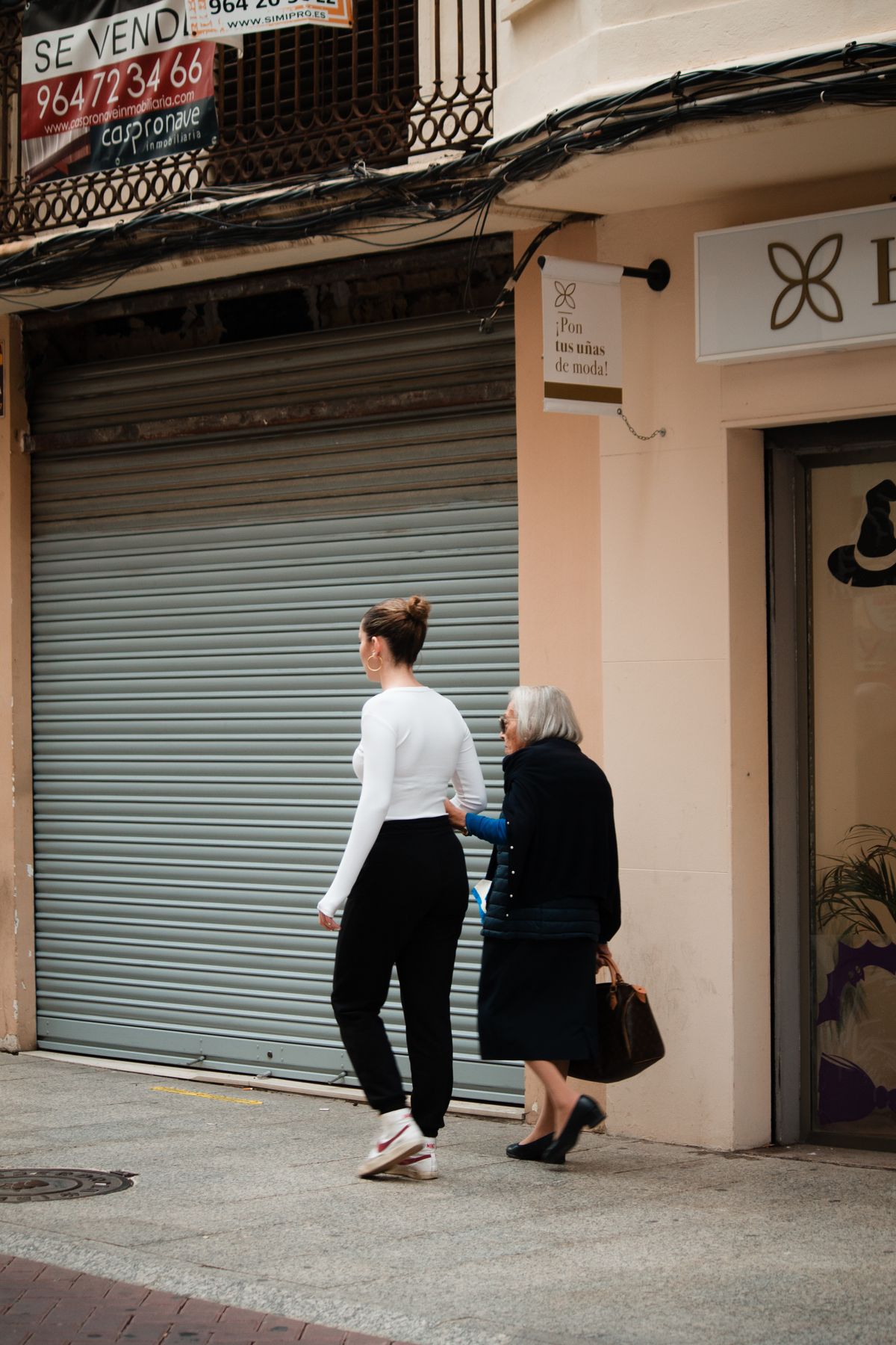 A woman helps an elderly woman walk on the sidewalk.