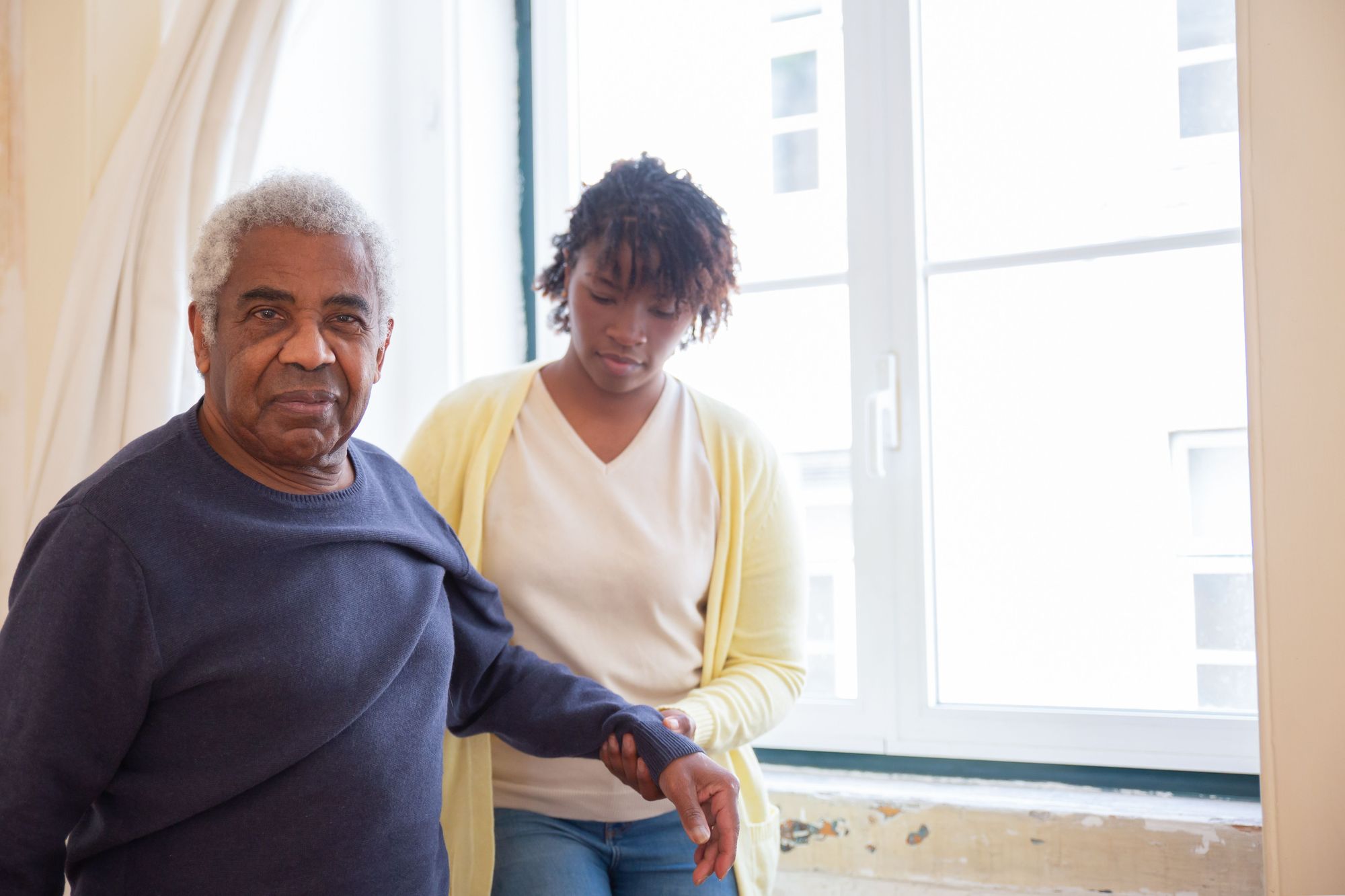 An aide steadying a client's arm by a window.