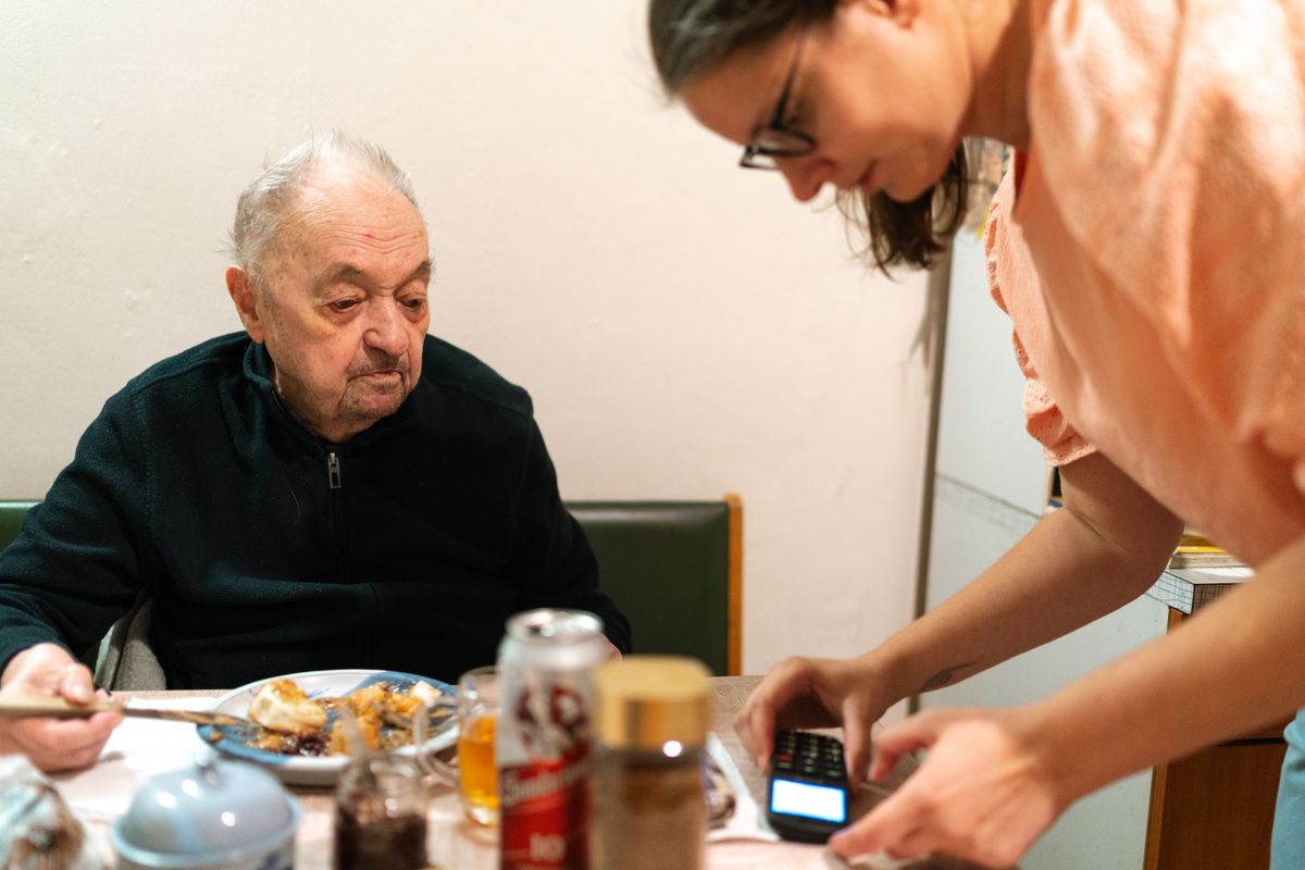 A caregiver tends to an elderly woman in a sunlit home kitchen — the everyday reality of NYC home care.
